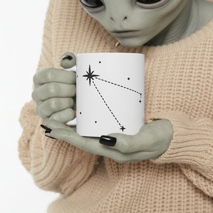 Person holding a mug with a star constellation design against a neutral background