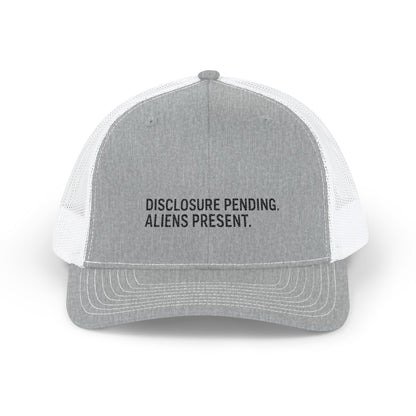 A light gray and white trucker hat with black text on the front panel reading 'DISCLOSURE PENDING. ALIENS PRESENT.