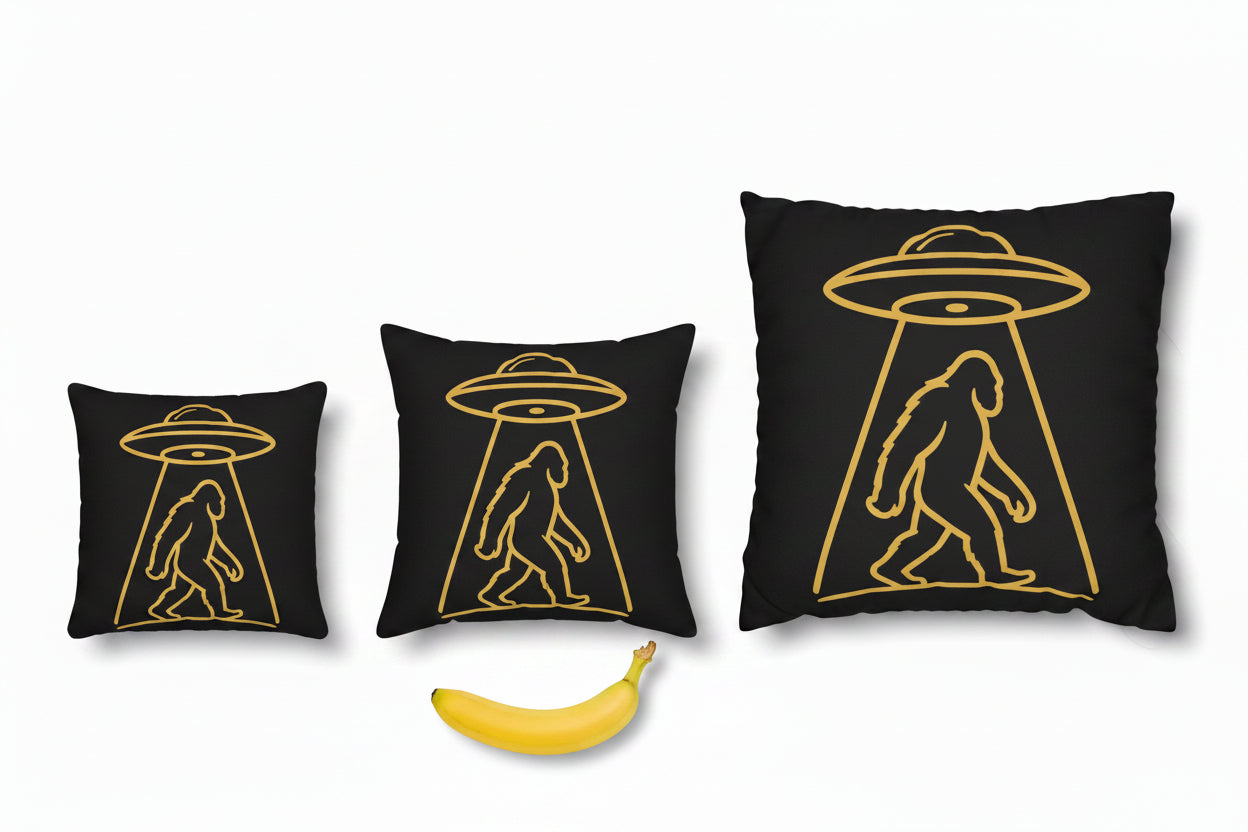 A square black throw pillow featuring a gold graphic of a walking Bigfoot silhouette under a flying saucer, shown against a plain white background.